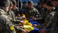 Ukrajinští vojáci rozbalují v Kyjevě státní vlajku nad rakví s ostatky svého spolubojovníka a biologa Bižana Šaropova