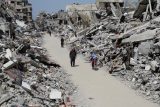 Palestinci procházejí kolem trosek domů a budov v severní části Pásma Gazy