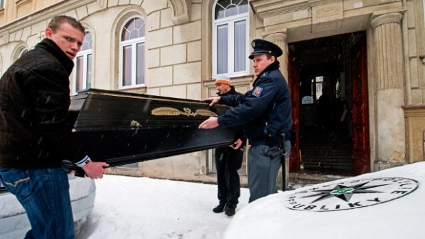 Pohřební služba vynáší tělo hudebníka v rakvi z domu, kde byl spolu s manželkou zavražděn.