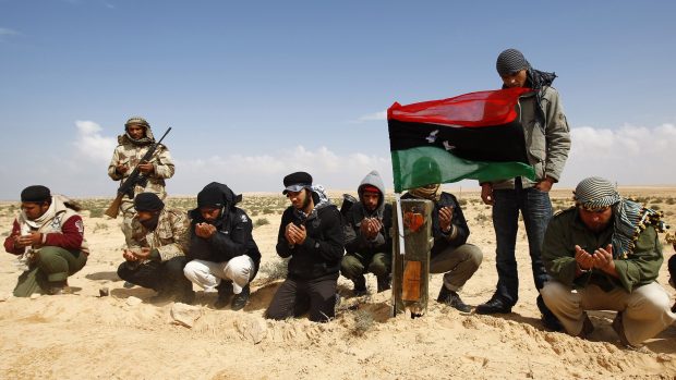 Libyjští povstalci se modlí u hrobu rebelů, kteří byli zabiti při útok na konvoj v okolí přístavu Brega