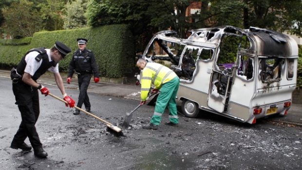 Policisté pomáhají odklízet zbytky vypáleného karavanu po násilnostech v Liverpoolu.