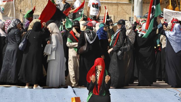 Žena se modlí, zatímco jiní oslavují konec Kaddáfího na náměstí v Tripolisu