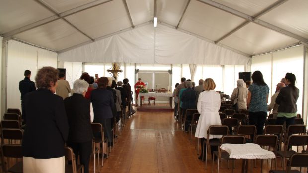 Lidé stojí během bohoslužby v improvizovaném stanu