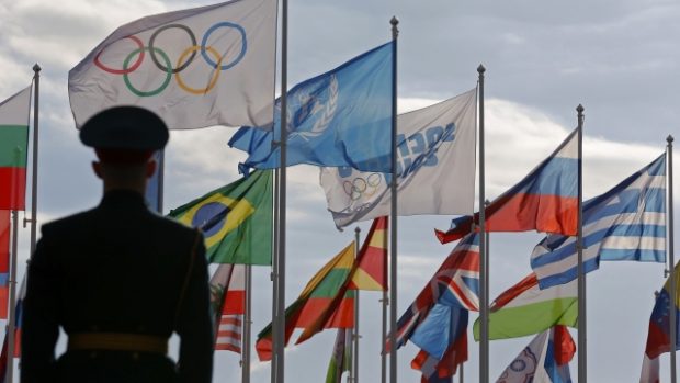 Ruský voják stojí před vlajkami v olympijské vesnici před zahájením zimních olympijských her v Soči