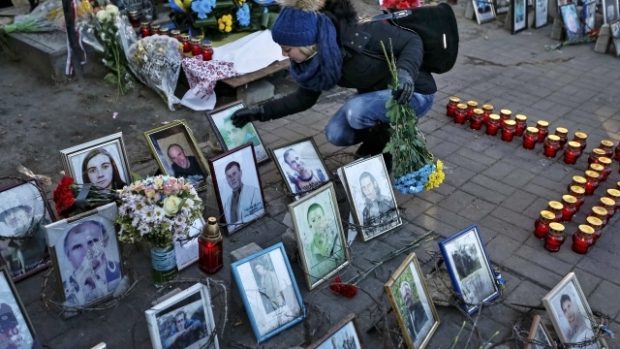 Dívka pokládá květiny k potrétům bojovníků zabitých před rokem při střetech v Kyjevě