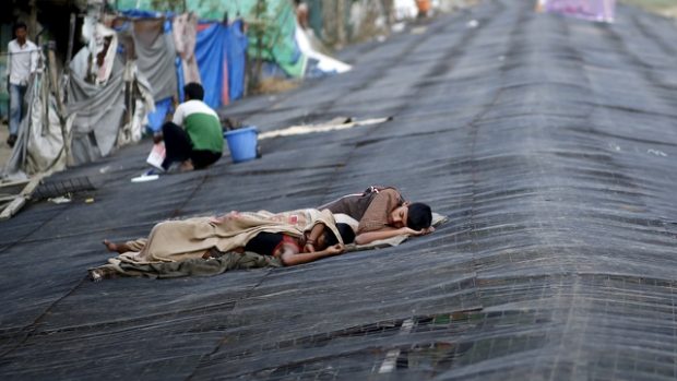 Indii sužuje vlna veder, muž odpočívá na plachtě vedle slumu