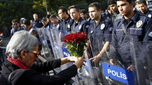 Postarší žena s květinami stojí před příslušníky turecké policie v Ankaře, kde si lidé připomněli oběti sobotního útoku