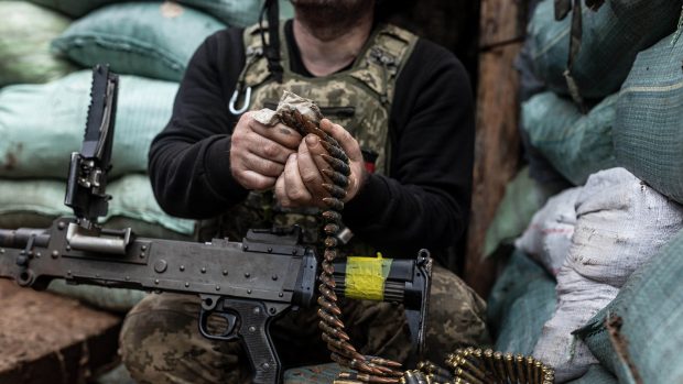 Ukrajinský voják nabíjí kulomet na bojové pozici v zákopu