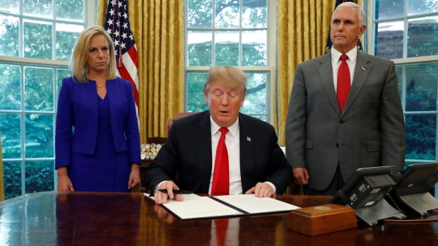 Americký prezident Donald Trump (uprostřed)  podpisuje migrační dekret. Přihlíží viceprezident Mike Pence (vpravo).