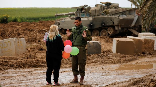 Žena dává poblíž hranice s Pásmem Gaza izraelskému vojákovi balónky, snímek agentury Reuters