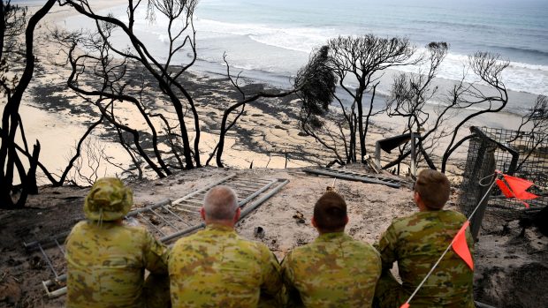 Vojáci sedící na pláži ve městě Mallacoota hledí na ohořelé stromy. Fotografie z 10. ledna