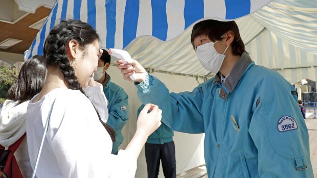 Zdravotník kontroluje teplotu lidí v japonském Tokiu
