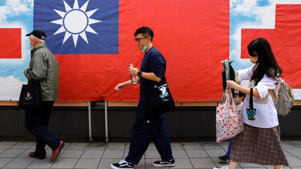 Lidé v Tchaj-peji procházejí kolem tchajwanské vlajky