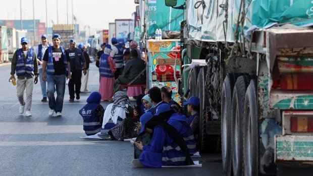 Egyptští dobrovolníci odpočívají u nákladních aut naložených humanitární pomocí u hraničního přechodu Rafah mezi Pásmem Gazy a Egyptem