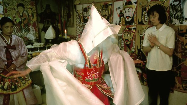 Velkou roli v korejské tradici hraje také šamanismus; obřady za duše zemřelých konali korejští šamani po staletí. Snímek zachycuje šamanku v Soulu při rituálu k navázání kontaktu se zesnulými předky.