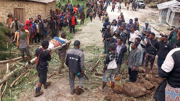 Fotografie Mezinárodní organizace pro migraci (IOM) z 25. května 2024 ukazuje, jak místní obyvatelé nesou osobu na nosítkách z místa sesuvu půdy ve vesnici Yambali v regionu Maip Mulitaka v provincii Enga na Papui Nové Guineji