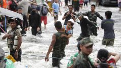 Thajský voják pomáhá chlapci přes proudící vodu na ulici v provincii Pathum Thani