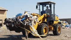 V betonové ohradě, v poušti kousek za Hurghádou, vysypává nakladač lžíci plnou pytlů s odpadky do úst recyklační linky.