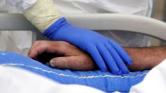 Zdravotník drží za ruku pacienta s koronavirem na jednotce intenzivní péče nemocnice ve Slaném