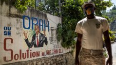 Haitský policista stojí před zdí s obrázkem zavražděného prezidenta