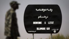 Voják kráčí u tabule s nápisem „Vítejte v Islámském státu Gao“ před maliským městem Gao (březen 2013)