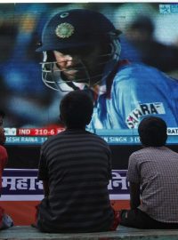 Děti sledují kriketový zápas na obří obrazovce.