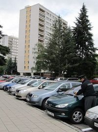 Automobily na parkovišti u panelového domu spolu s policejní hlídkou