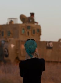 Žena si fotografuje izraelské vojáky blízko hranice s Gazou