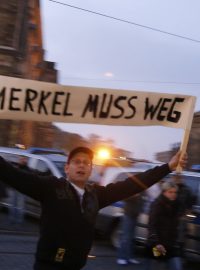 Rok od vzniku hnutí Pegida se v Drážďanech demonstruje. Muž drží transparent s nápisem Merkelová musí pryč