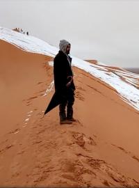 Muž hledí na zasněženou písečnou dunu v Alžírsku