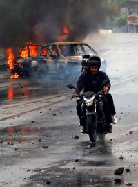 Policista míří zbraní na muže na motorce během protestů proti nikaragujskému prezidentovi Danielu Ortegovi