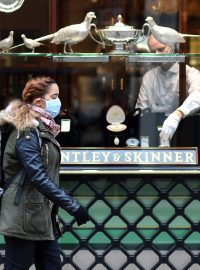 Žena s rouškou před obchodem v centru Londýna na Piccadilly Circus